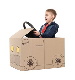 Photo of Little boy driving car made of cardboard on white background