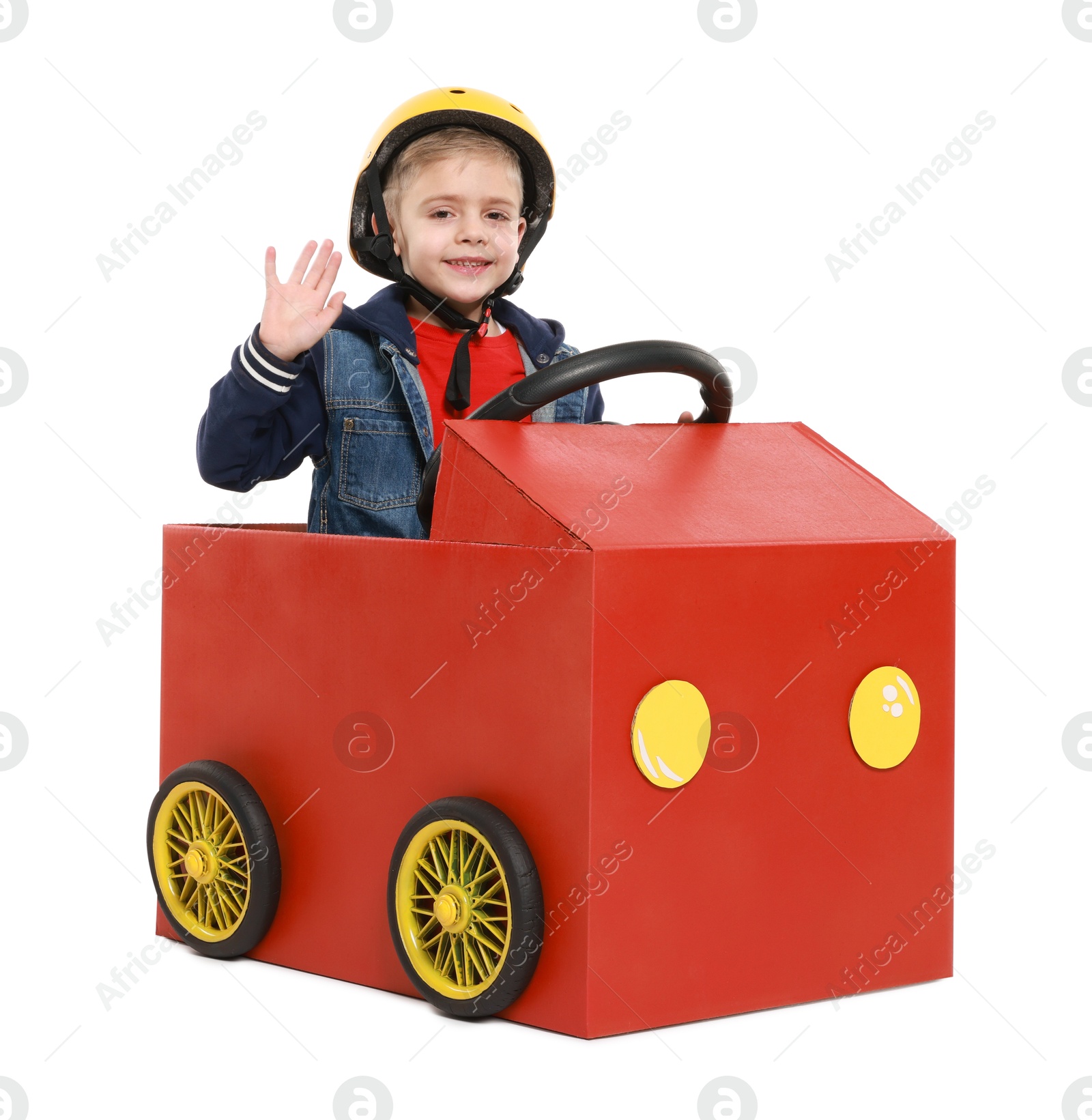 Photo of Little boy waving while driving car made of cardboard on white background