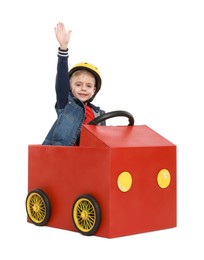 Little boy waving while driving car made of cardboard on white background