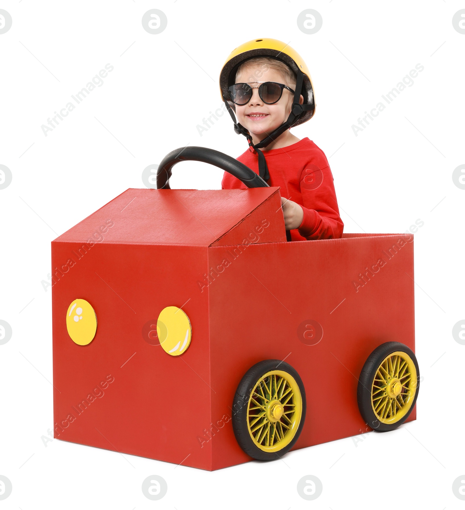 Photo of Little boy driving car made of cardboard on white background