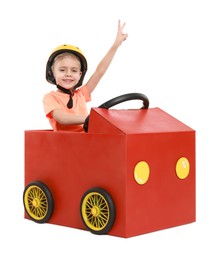 Photo of Little boy showing V-sign while driving car made of cardboard on white background