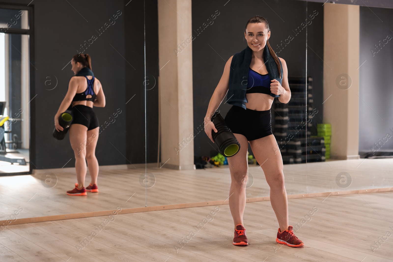 Photo of Happy woman with towel and foam roller in fitness studio