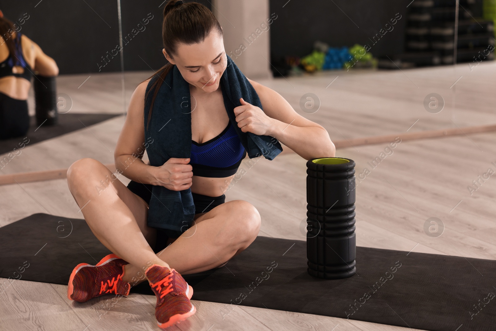 Photo of Happy woman with towel and foam roller on mat in fitness studio