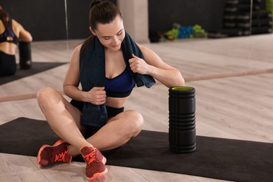 Photo of Happy woman with towel and foam roller on mat in fitness studio