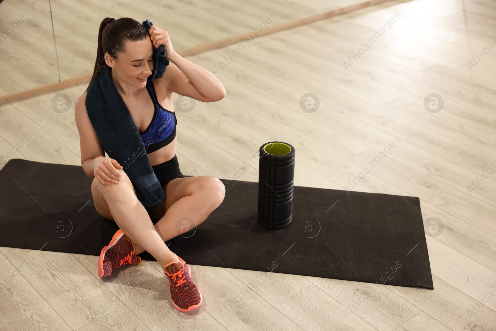 Photo of Happy woman with towel and foam roller on mat in fitness studio. Space for text