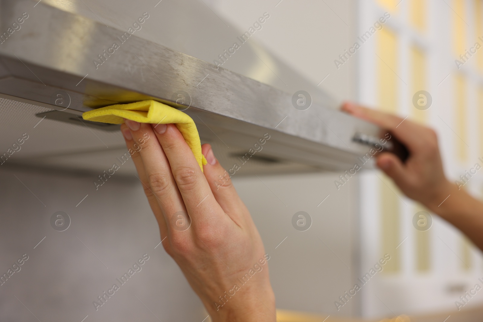 Photo of Man cleaning kitchen hood with rag indoors, closeup