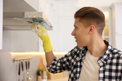 Photo of Man cleaning kitchen hood with sponge at home