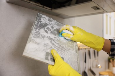 Photo of Man cleaning filter of kitchen hood with sponge indoors, closeup