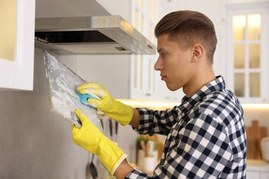 Man cleaning filter of kitchen hood with sponge indoors