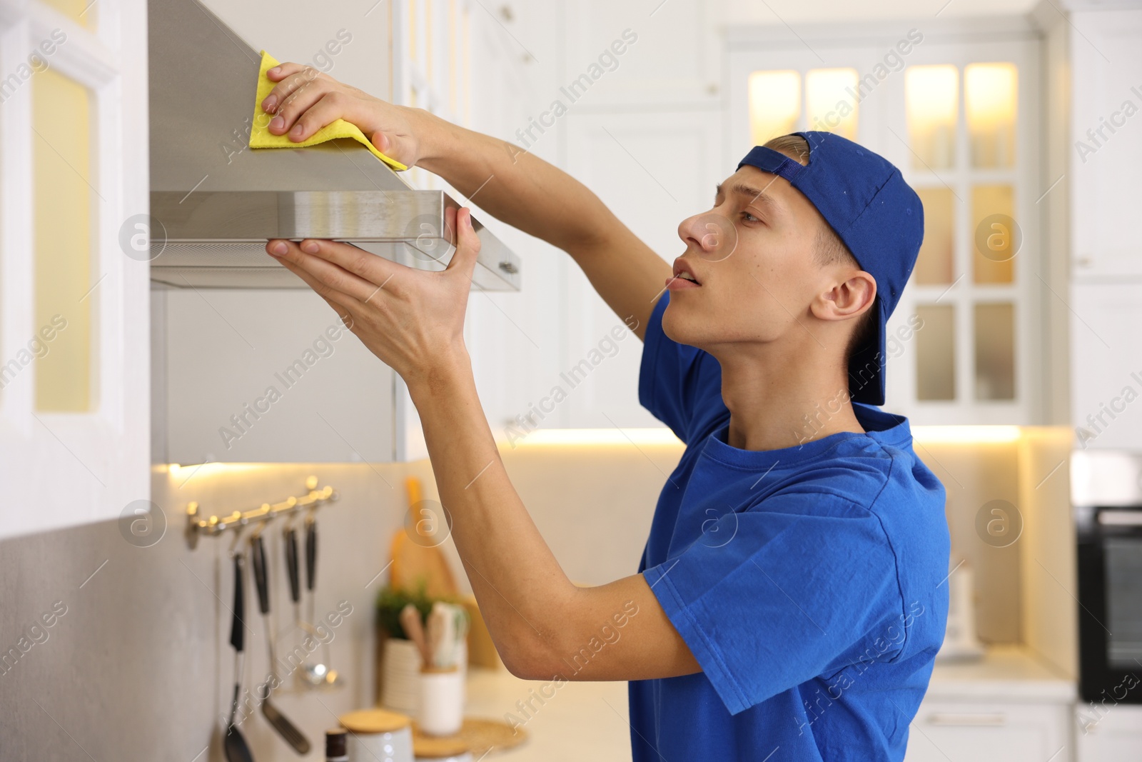 Photo of Professional janitor cleaning kitchen hood with rag indoors