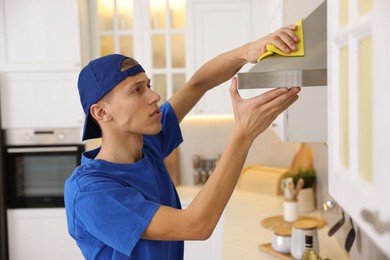 Photo of Professional janitor cleaning kitchen hood with rag indoors