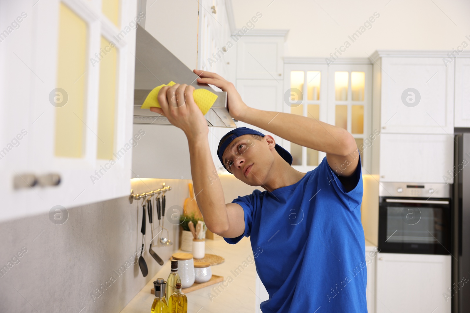 Photo of Professional janitor cleaning kitchen hood with rag indoors