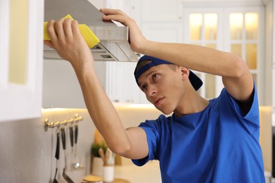 Photo of Professional janitor cleaning kitchen hood with rag indoors