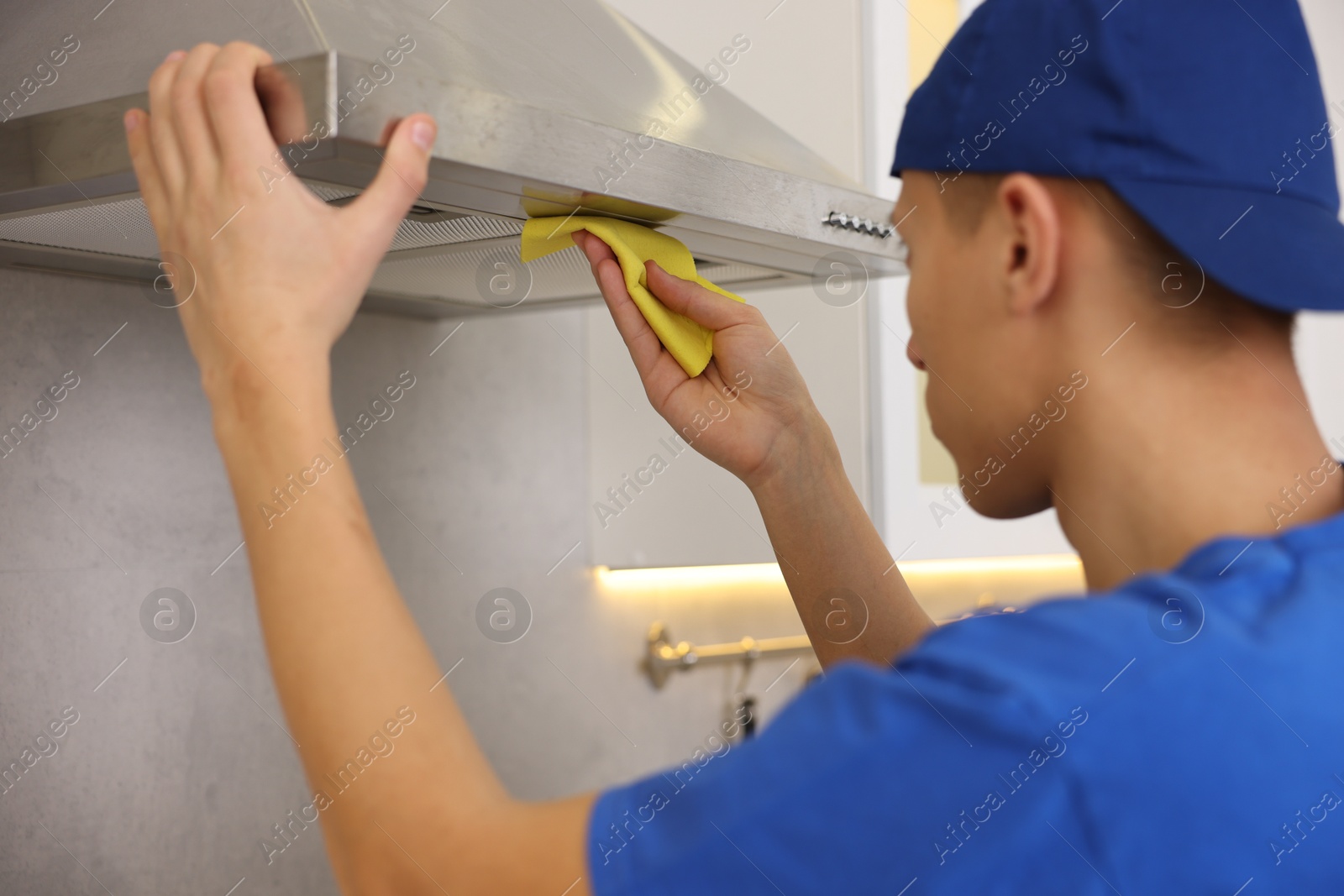 Photo of Professional janitor cleaning kitchen hood with rag indoors