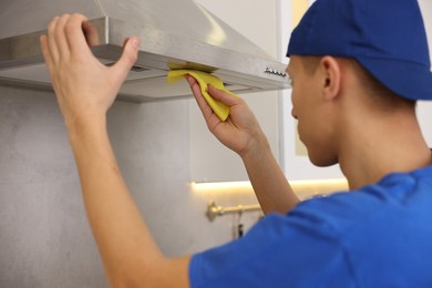 Photo of Professional janitor cleaning kitchen hood with rag indoors