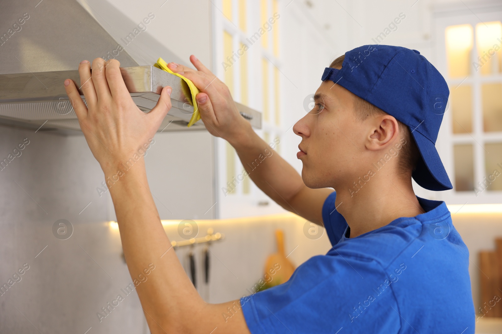 Photo of Professional janitor cleaning kitchen hood with rag indoors