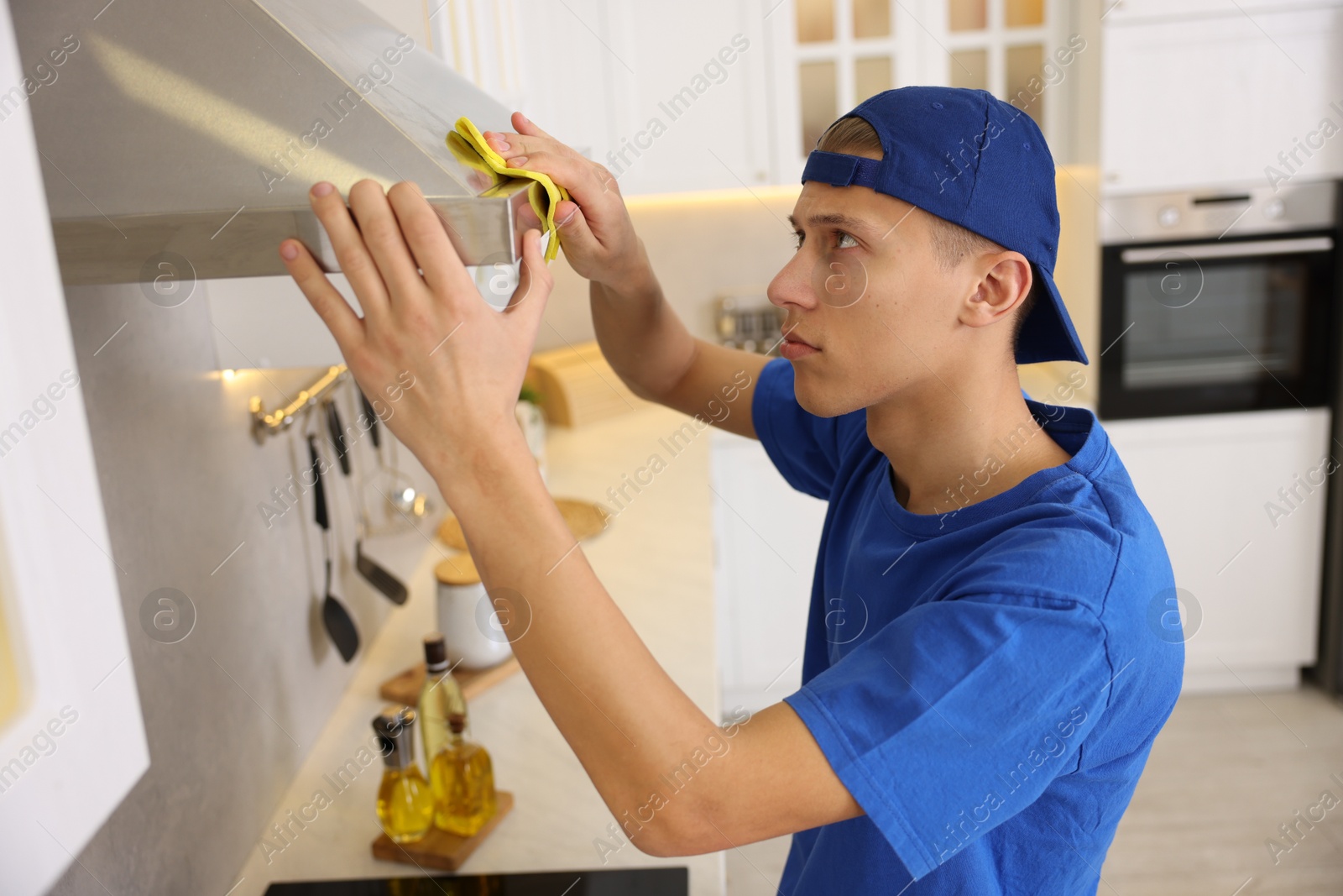 Photo of Professional janitor cleaning kitchen hood with rag indoors