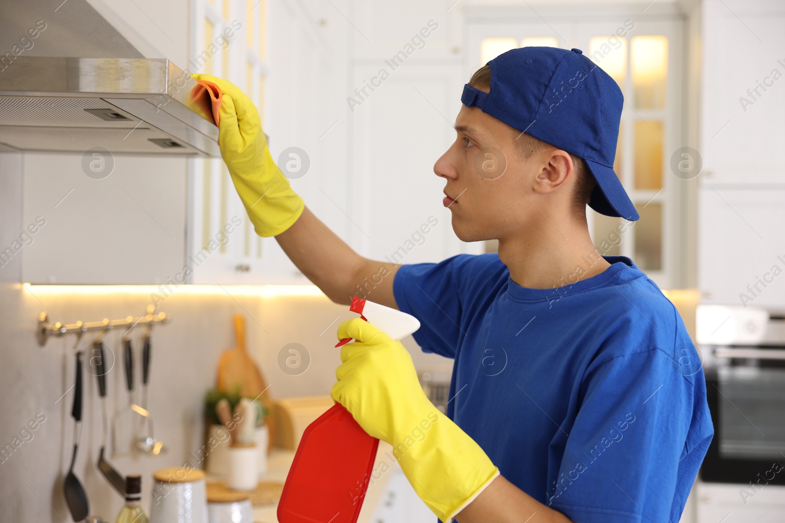 Photo of Professional janitor cleaning kitchen hood with rag and detergent indoors