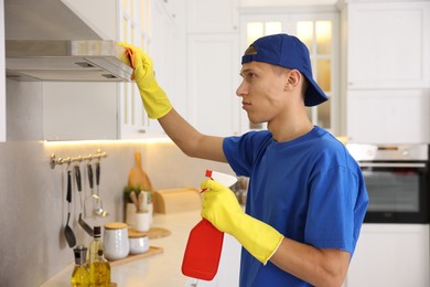 Professional janitor cleaning kitchen hood with rag and detergent indoors