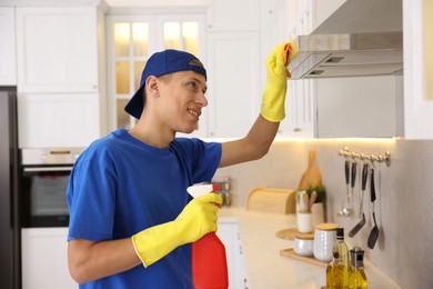 Photo of Professional janitor cleaning kitchen hood with rag and detergent indoors