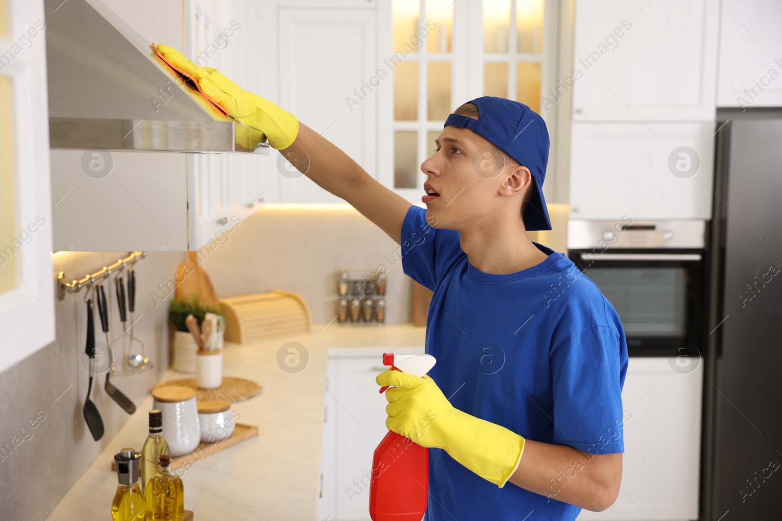 Photo of Professional janitor cleaning kitchen hood with rag and detergent indoors