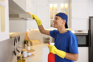 Photo of Professional janitor cleaning kitchen hood with rag and detergent indoors