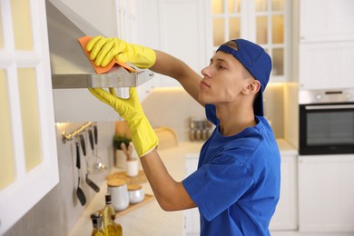 Photo of Professional janitor cleaning kitchen hood with rag indoors