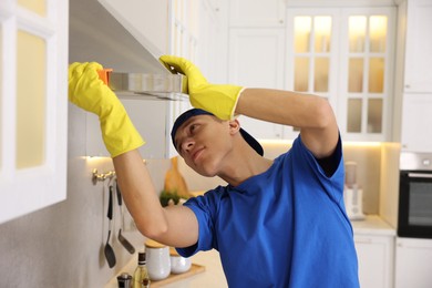 Professional janitor cleaning kitchen hood with rag indoors