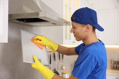 Photo of Professional janitor cleaning filter of kitchen hood with rag indoors