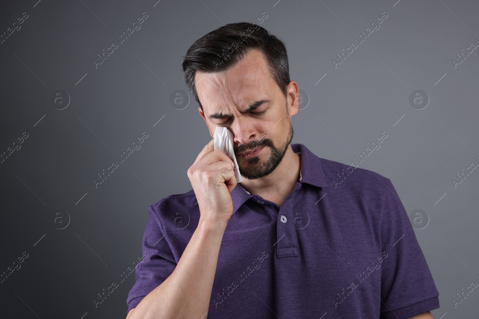 Photo of Sad man with paper tissue crying on grey background, space for text