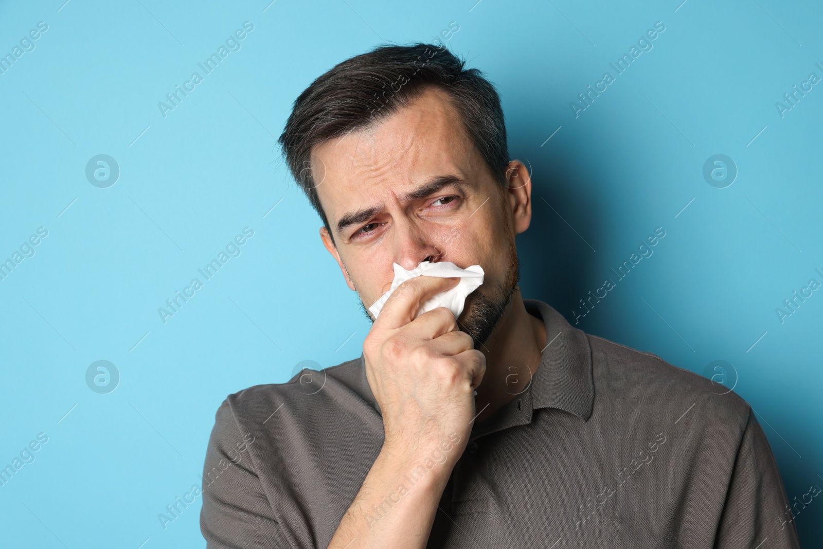 Photo of Sad man with paper tissue crying on light blue background