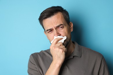 Sad man with paper tissue crying on light blue background