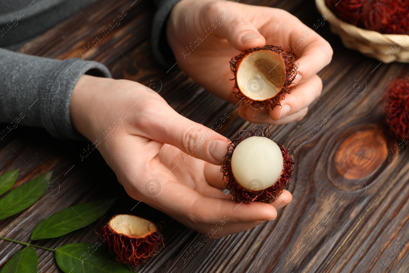 Photo of Woman peeling ripe rambutan at wooden table, closeup