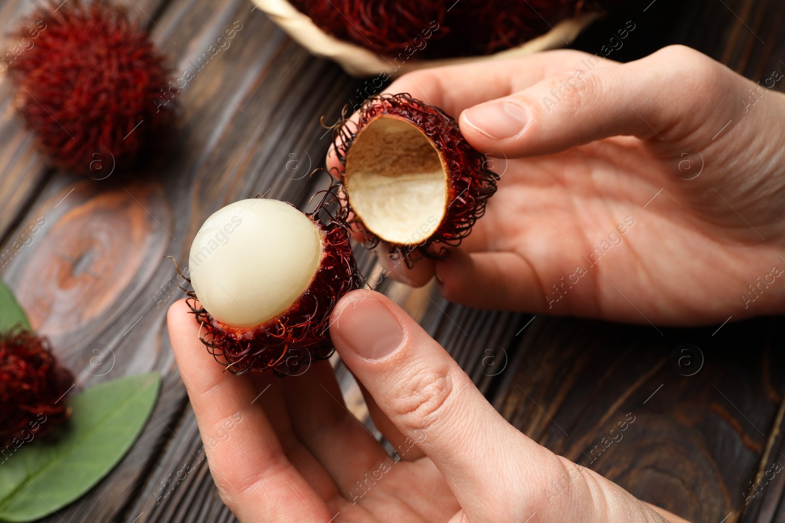 Photo of Woman peeling ripe rambutan at wooden table, closeup