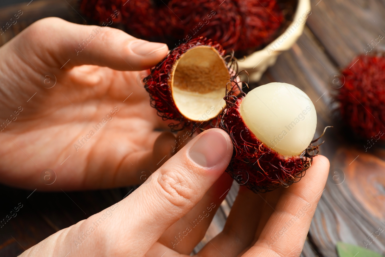 Photo of Woman peeling ripe rambutan at wooden table, closeup