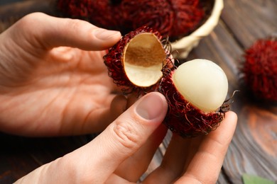 Photo of Woman peeling ripe rambutan at wooden table, closeup