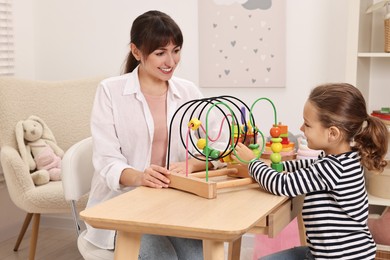 Photo of Autism therapy. Smiling psychologist and little girl playing with educational toy at table in mental health center