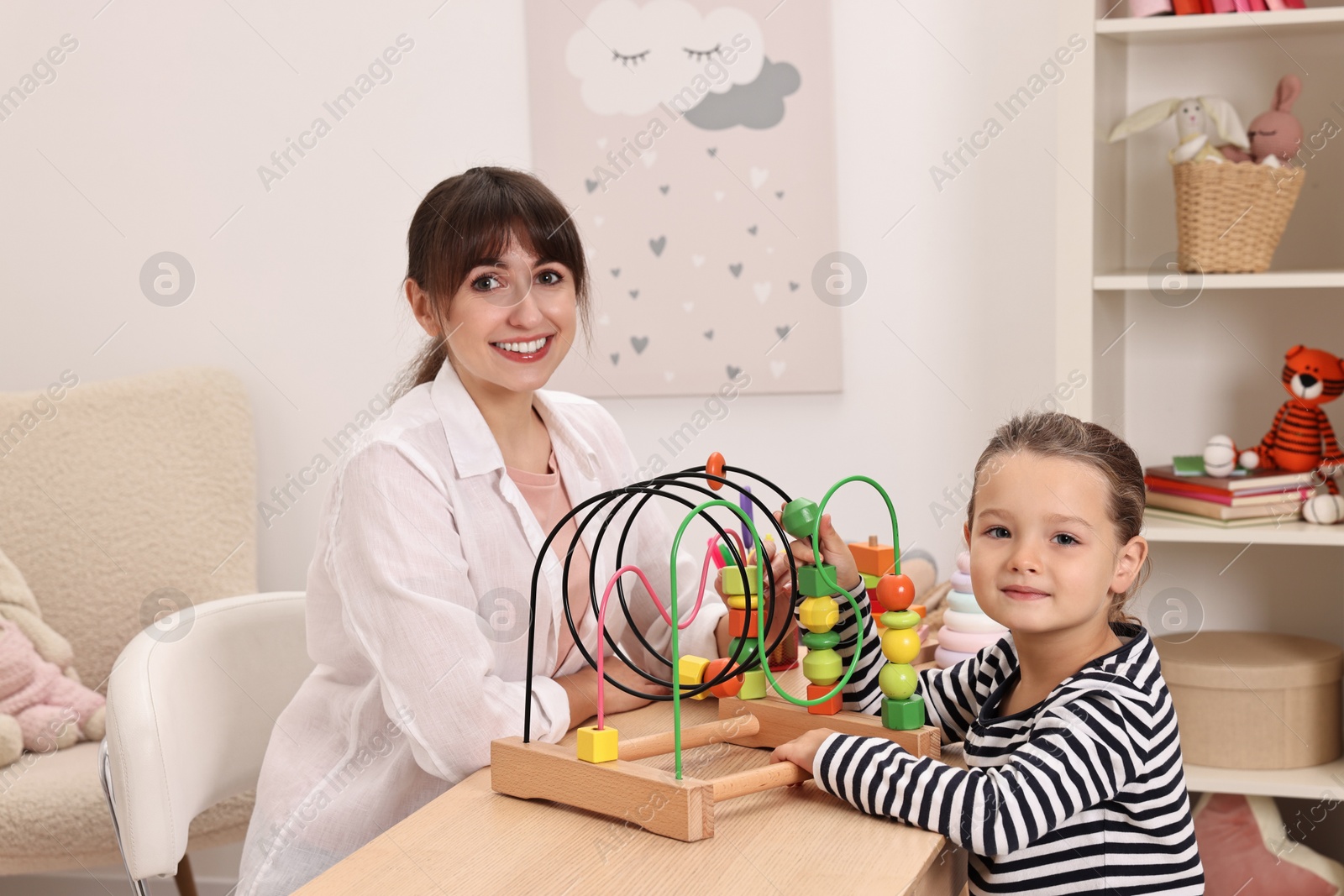 Photo of Autism therapy. Smiling psychologist and little girl playing with educational toy at table in mental health center