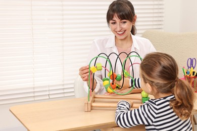 Autism therapy. Smiling psychologist and little girl playing with educational toy at table in mental health center, space for text