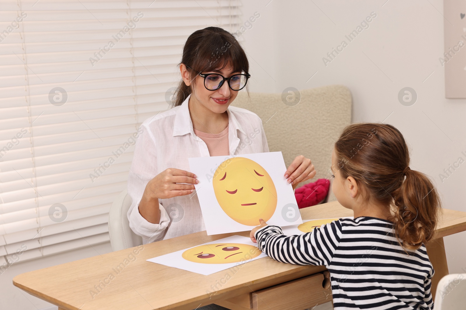 Photo of Autism therapy. Little girl choosing emoticon at table with psychologist in mental health center