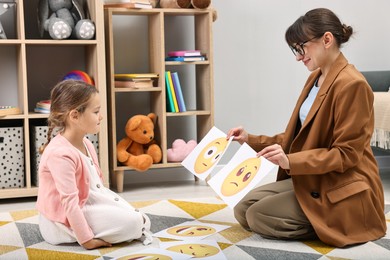 Photo of Autism therapy. Little girl choosing emoticon with psychologist in mental health center