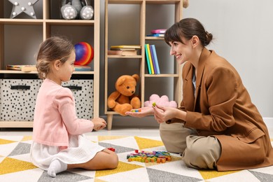 Photo of Autism therapy. Smiling psychologist and little girl playing with educational toy in mental health center