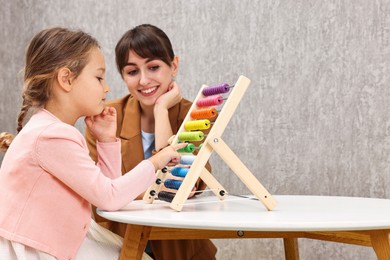 Photo of Autism therapy. Smiling psychologist and girl playing with wooden abacus indoors