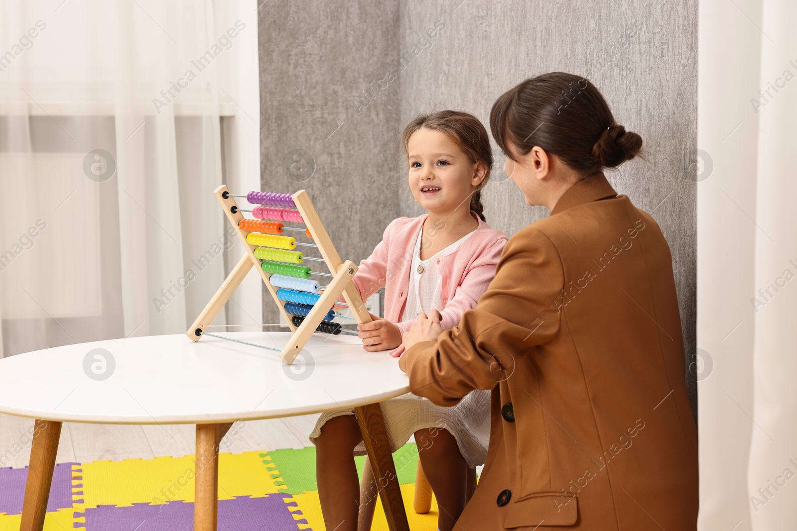 Photo of Autism therapy. Psychologist and smiling girl playing with wooden abacus at table indoors