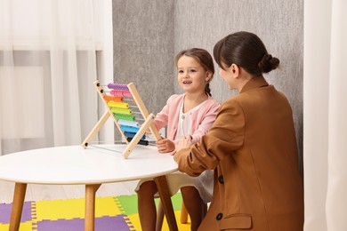 Autism therapy. Psychologist and smiling girl playing with wooden abacus at table indoors