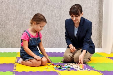 Photo of Autism therapy. Smiling psychologist and little girl playing with educational toy in mental health center