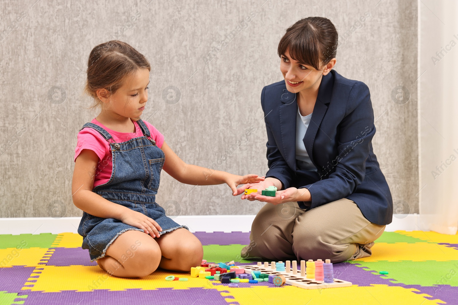 Photo of Autism therapy. Smiling psychologist and little girl playing with educational toy in mental health center