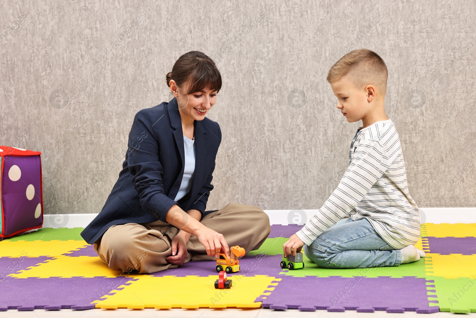 Photo of Autism therapy. Smiling psychologist and little boy playing with toy cars in mental health center