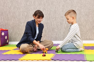 Photo of Autism therapy. Smiling psychologist and little boy playing with toy cars in mental health center