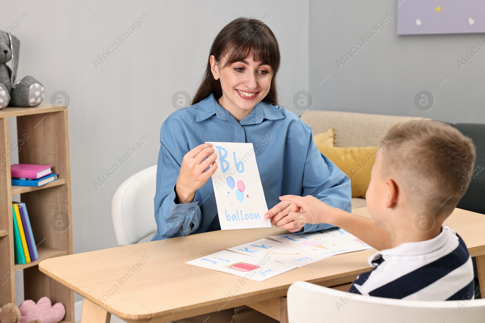 Photo of Smiling speech therapist working with little boy at table in autism treatment center